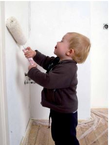 small child with paint roller painting wall in house